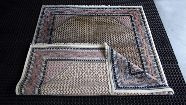 a folded indian mir rug on black cleaning mats