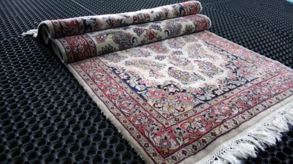 a folded qom rug on a black cleaning mat